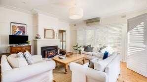 A living room with white furniture, a fireplace, and a television.