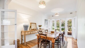A dining area with a wooden table, chairs, and a rug. There is a window with blinds, a door, and a wall-mounted lamp.