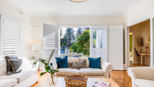 A living room with a beige sofa, a coffee table, and a view of greenery outside.
