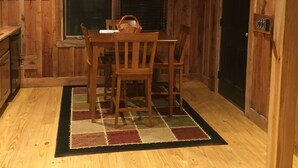 Interior em madeira com mesa de jantar, cadeiras, tapete e luminária pendente.