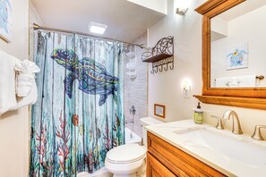 Een badkamer met douchegordijn met een kleurrijk zeeschild ontwerp, een wit toilet, een houten wastafelmeubel met een wastafel en een spiegel.