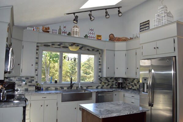 A modern kitchen with white cabinets, a stainless steel refrigerator, and a large window with a view of trees.