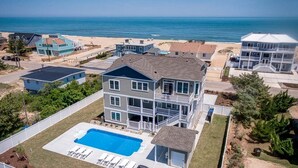 Une maison à plusieurs étages avec un grand jardin devant, une piscine et une vue sur l’océan.