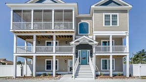 Une maison à deux étages située en bord de mer, dotée d’un balcon, d’une porte d’entrée et d’un escalier menant à l’entrée.