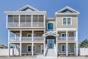 Ein zweistöckiges Strandhaus mit Balkon, einer Haustür und einer Treppe, die zum Eingang führt.