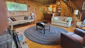 Een knus interieur van een chalet met houten details, een bank, een ronde salontafel en een trap.