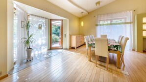 Un vaste espace dédié à la salle à manger, doté d’un plancher en bois, d’une table à manger avec des chaises et d’une plante en pot.