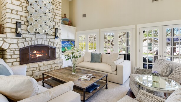 A living room with a stone fireplace, a white sofa, a coffee table, and large windows with a view of the outdoors. - Above Auth Westlake I Pool I Hot Tub I Game Room I Back House I Greenbelt (West Lake Hills)