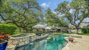 A swimming pool with a stone border, surrounded by a patio area with lounge chairs and a small waterfall feature. - Above Auth Westlake I Pool I Hot Tub I Game Room I Back House I Greenbelt (West Lake Hills)