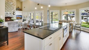 A spacious kitchen with a central island, white cabinetry, and a stone fireplace. - Above Auth Westlake I Pool I Hot Tub I Game Room I Back House I Greenbelt (West Lake Hills)