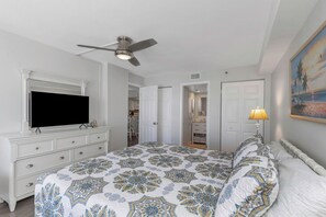 A bedroom with a bed, a television, a ceiling fan, a dresser, and a painting on the wall.