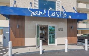 A hotel entrance with a blue awning and a sign that reads 'Sand Castle II'. - Gorgeous DIRECT BEACHFRONT 3/2 Condo Recliners, Pool, Hot Tub, Resort Amenities! (Indian Rocks Beach)