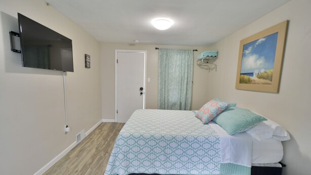 A bedroom with a bed, a television mounted on the wall, a door, and a painting. - Whitehall Cottages Boutique Motel - Full Bed (Whitehall)