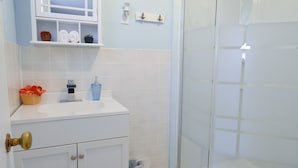 A bathroom with a white vanity, a glass shower enclosure, and a tiled floor. - Whitehall Cottages Boutique Motel - Full Bed (Whitehall)