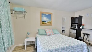 A bedroom with a bed, a nightstand, a desk, a hanging towel rack, a painting, a microwave, and a refrigerator. - Whitehall Cottages Boutique Motel - Full Bed (Whitehall)