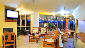 A spacious lobby with wooden furniture, a flat-screen TV, and large windows with blue lighting. - Hotel Costanera (Villa Carlos Paz)
