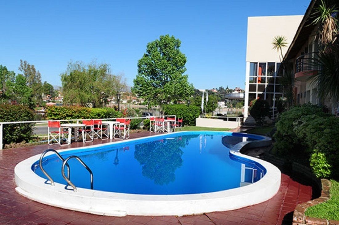 Una piscina con deck blanco, rodeada de follaje y un edificio con amplios ventanales.