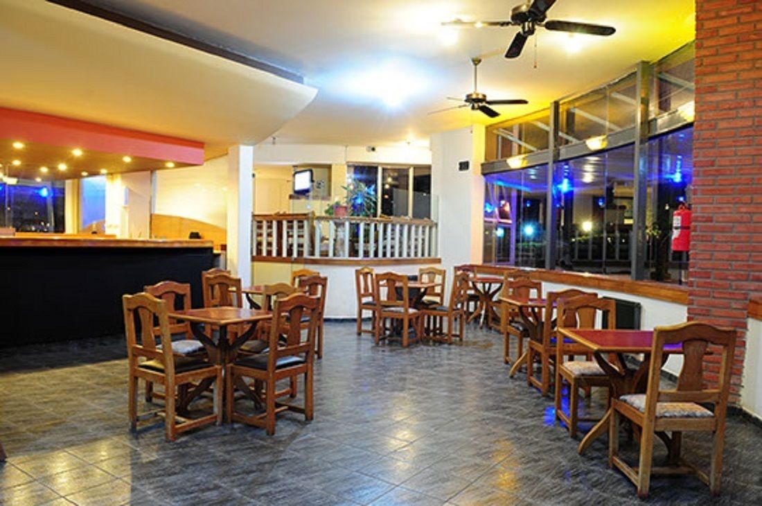Un restaurante con mesas y sillas de madera, una zona de bar y grandes ventanales con vistas.