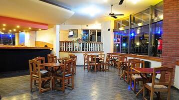 Un restaurante con mesas y sillas de madera, una zona de bar y grandes ventanales con vistas.