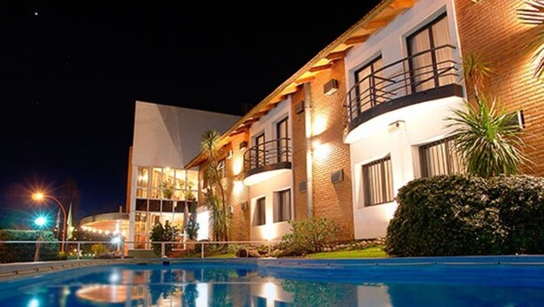 A modern hotel with a swimming pool, a well-lit exterior, and a mix of brick and glass architecture. - Hotel Costanera (Villa Carlos Paz)