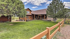 A log cabin with a covered patio, surrounded by a wooden fence and trees.
