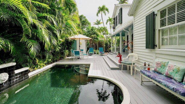 A pool area with a wooden deck, lounge chairs, and a small table.