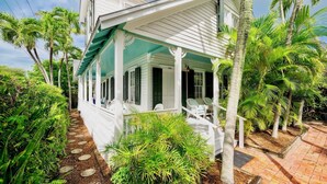 A white colonial-style house with a covered porch, palm trees, and a brick pathway.