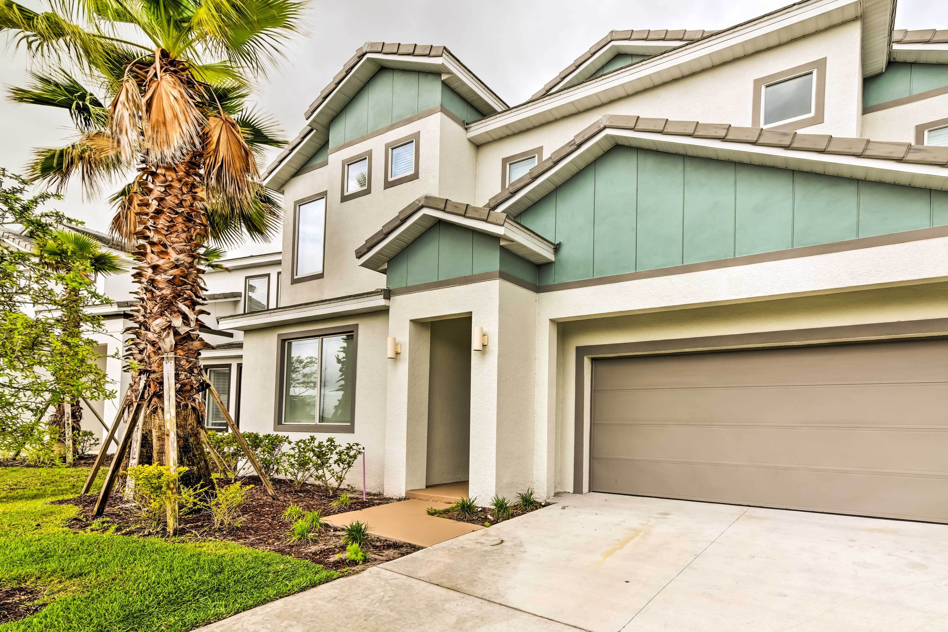 A modern two-story house with a garage, a well-maintained lawn, and a palm tree.