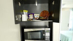 Una kitchenette compacta con microondas, refrigerador y una repisa superior con aperitivos y una cesta.