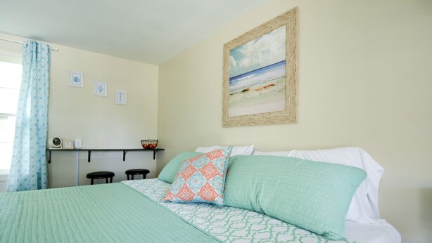Un dormitorio con cama, estante decorado con objetos y una pintura de playa en la pared.