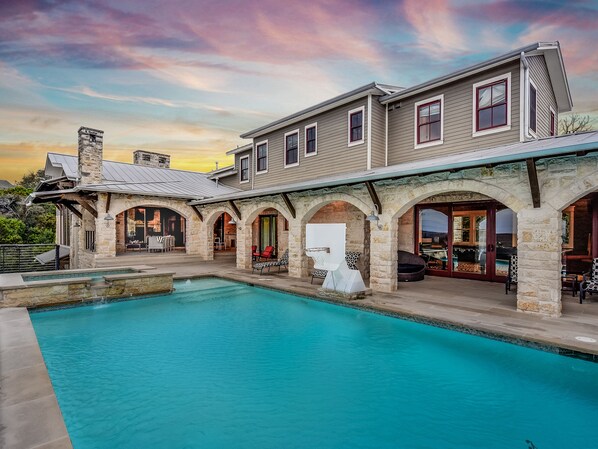 A large house with a swimming pool, stone arches, and a stone chimney.