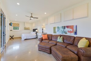 A spacious living room with a brown leather sofa, a white bed, and a ceiling fan. - Above Canyon View I Game Room | Pool I Hot Tub I Views I Family (Austin)