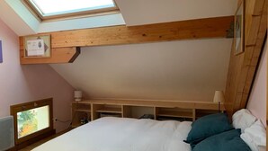 Un dormitorio con tragaluces, una cama con ropa de cama blanca y turquesa, y vigas de madera en el techo.