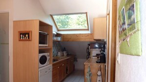 Cocina compacta con armarios de madera, microondas integrado y una pequeña zona de comedor con dos sillas.