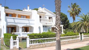 Un bâtiment blanc à deux étages, doté de balcons, d’un mur en pierre et d’une clôture blanche.