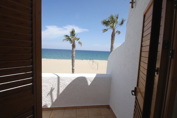 A view from a balcony overlooking a beach with two palm trees and a clear sky.