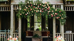 A wooden building with a porch adorned with a floral arch. - Roanoke Island Inn (Manteo)