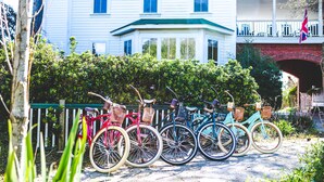 A row of bicycles parked in front of a house with a porch and a flag. - Roanoke Island Inn (Manteo)