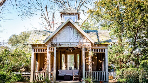 A wooden cabin with a porch, a small staircase, and a window overlooking a garden. - Roanoke Island Inn (Manteo)