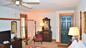 A hotel room with a bed, a dresser, a chair, a desk, a ceiling fan, a door, and a window with blinds.