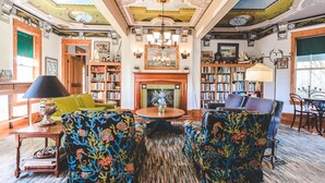 A spacious living room with a fireplace, bookshelves, and a chandelier. - Roanoke Island Inn (Manteo)