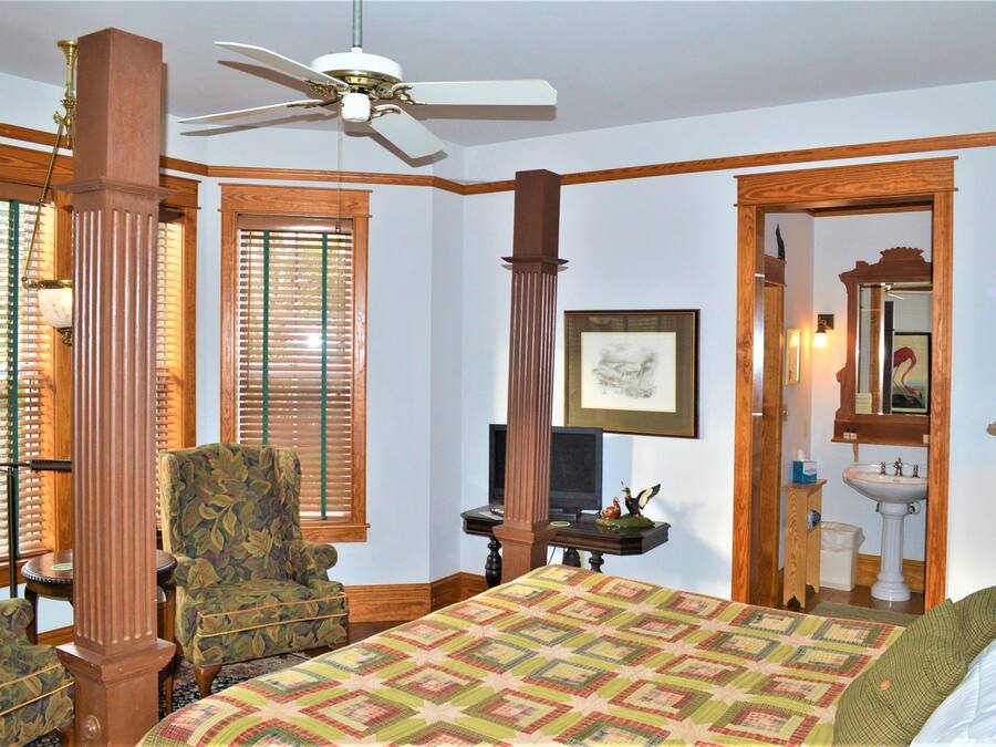 A bedroom with a bed, a chair, a television, a ceiling fan, and wooden trim.