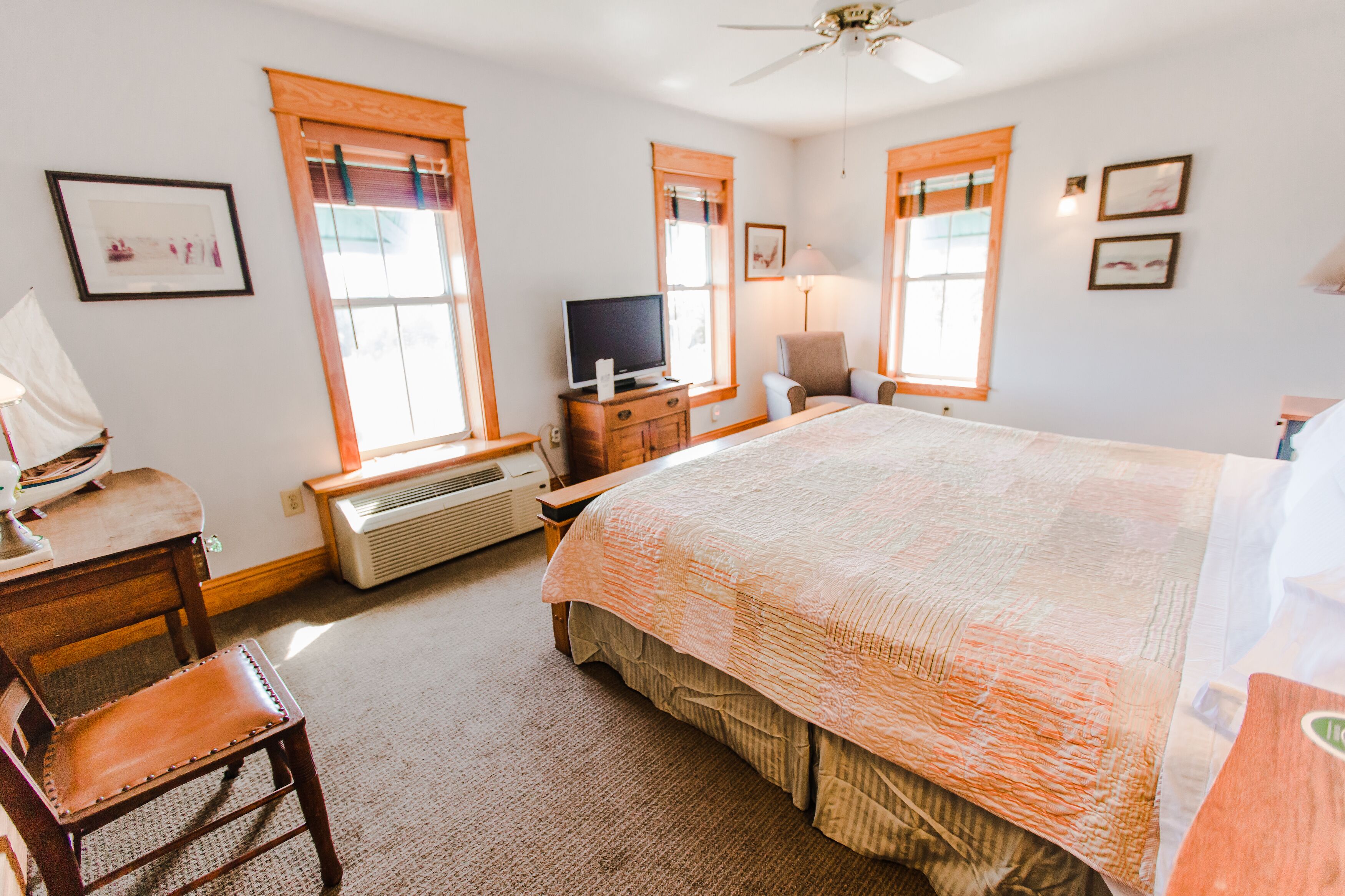 A bedroom with a large bed, a desk with a chair, a television, and a window with blinds.