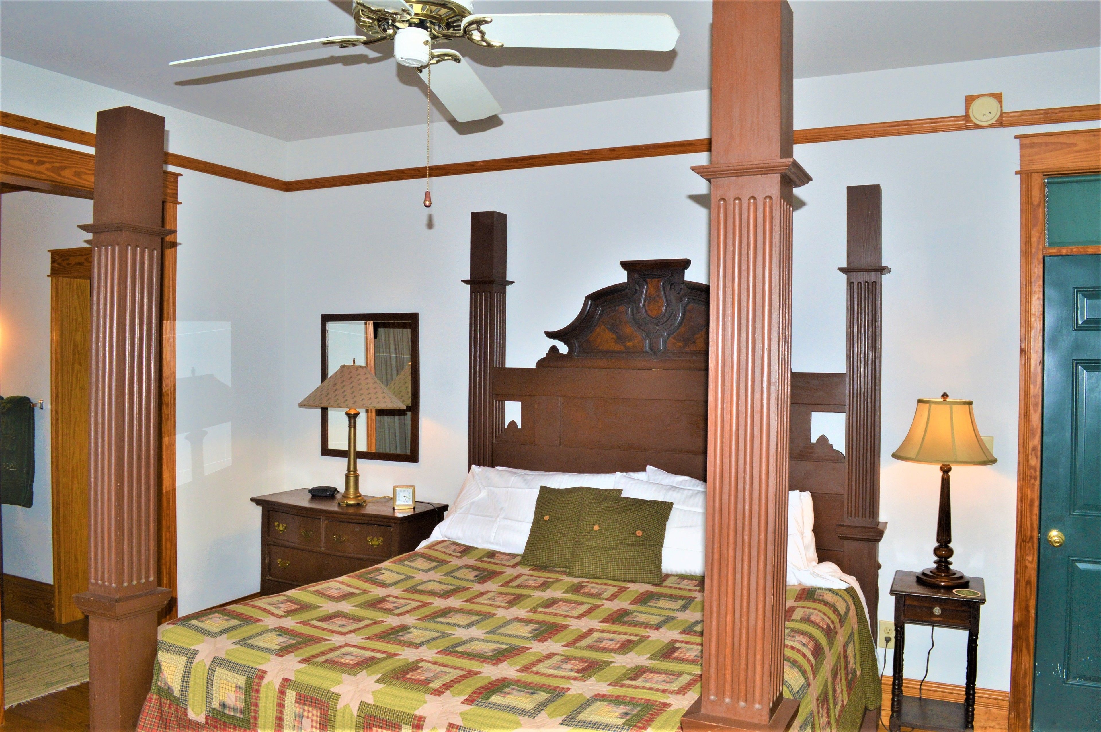 A bedroom with a four-poster bed, wooden headboard, and a ceiling fan.