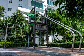 Un'area giochi con strutture per arrampicata e altalene, immersa nel verde con un edificio sullo sfondo.