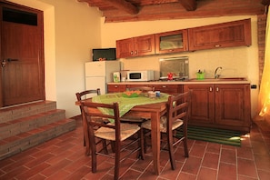 Una cocina con armarios de madera, un refrigerador blanco, un microondas y un lavamanos. Hay una mesa de comedor con sillas y un mantel verde.