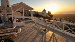 Une terrasse sur le toit, agrémentée d’une pergola, de chaises longues et offrant une vue sur un bâtiment blanc doté d’un dôme et d’un clocher, le tout illuminé par les couleurs du coucher de soleil.