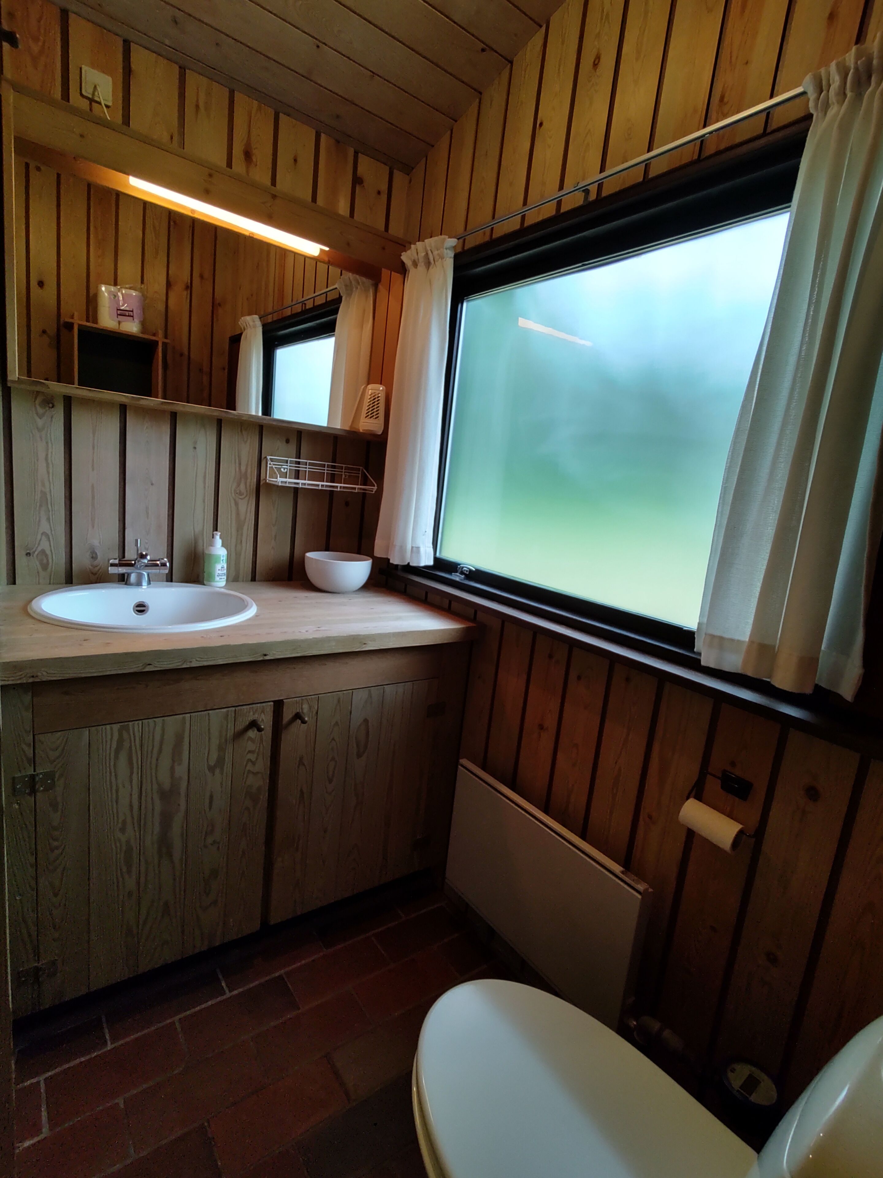 A wooden cabin bathroom with a sink, mirror, and window.