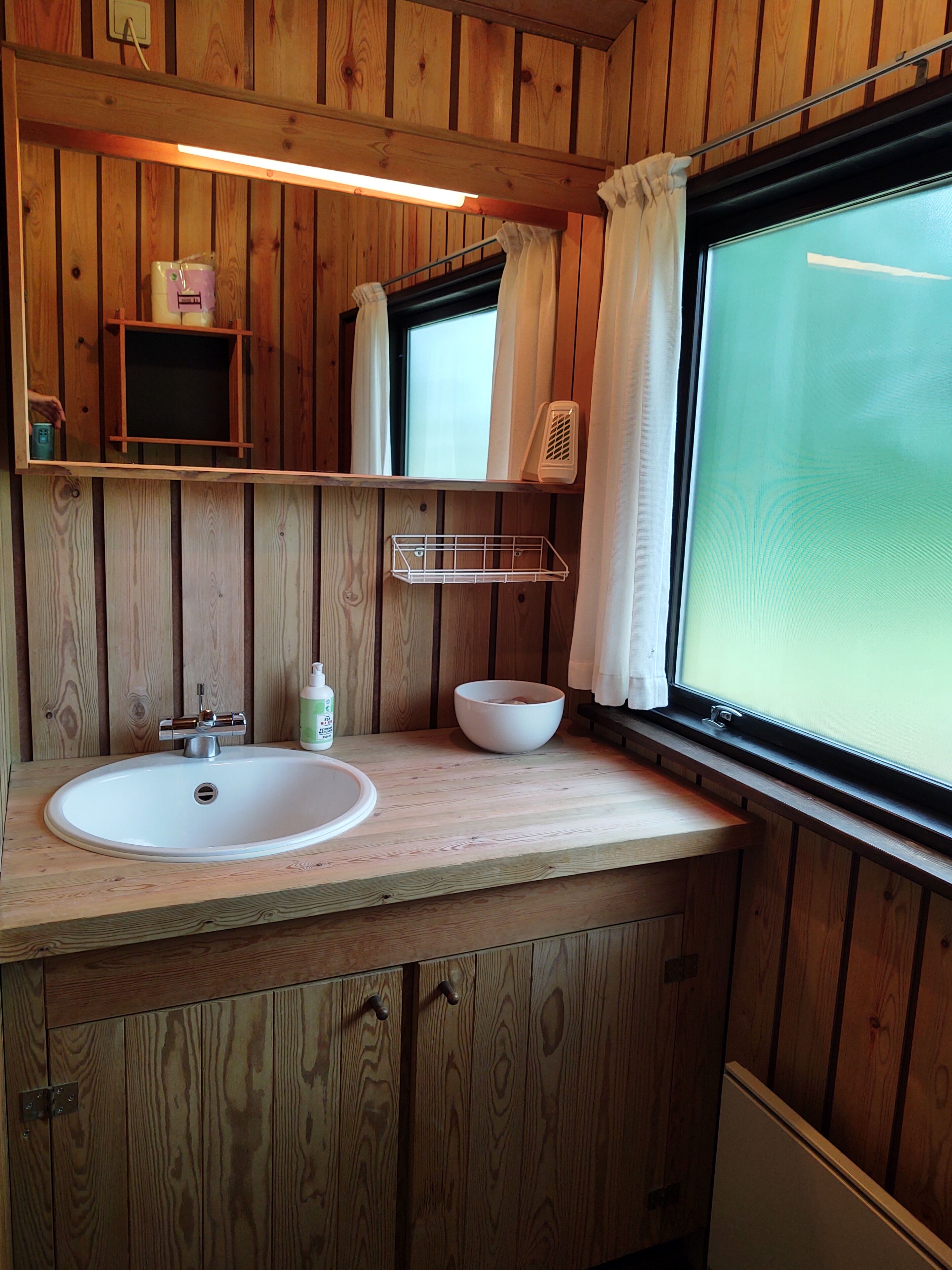 A wooden cabin bathroom with a sink, mirror, and window.