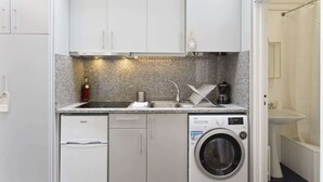 Une cuisine compacte équipée d’un lave-linge, d’un lave-vaisselle et d’un plan de travail sur lequel se trouvent une bouteille et une machine à café.